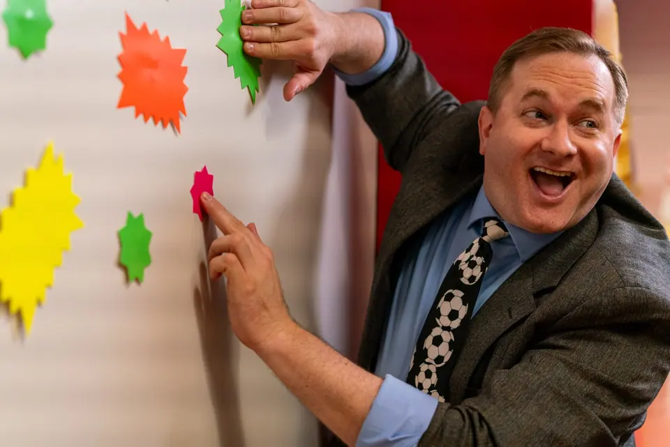 Performer delivering a comic reaction on a colorful practical set